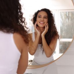 young woman looking in mirror considering options for preventative aesthetics